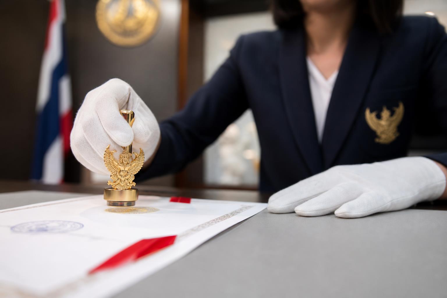 นิติกรณ์กรมการกงสุล — Thai Ministry of Foreign Affairs consular officer embossing a Garuda seal on a legalized document with red ribbon